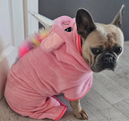 Frenchie wearing a pink unicorn costume on a wooden floor.
