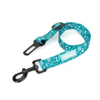 A teal seat belt restraint for dogs with a pattern of white paw prints and text, featuring adjustable straps and a clip buckle.