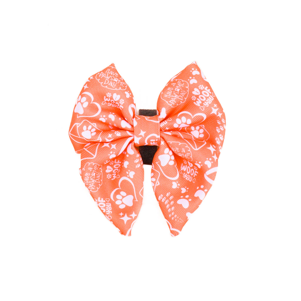 An orange dog sailor bowtie with a pattern that includes paw prints and illustrations.